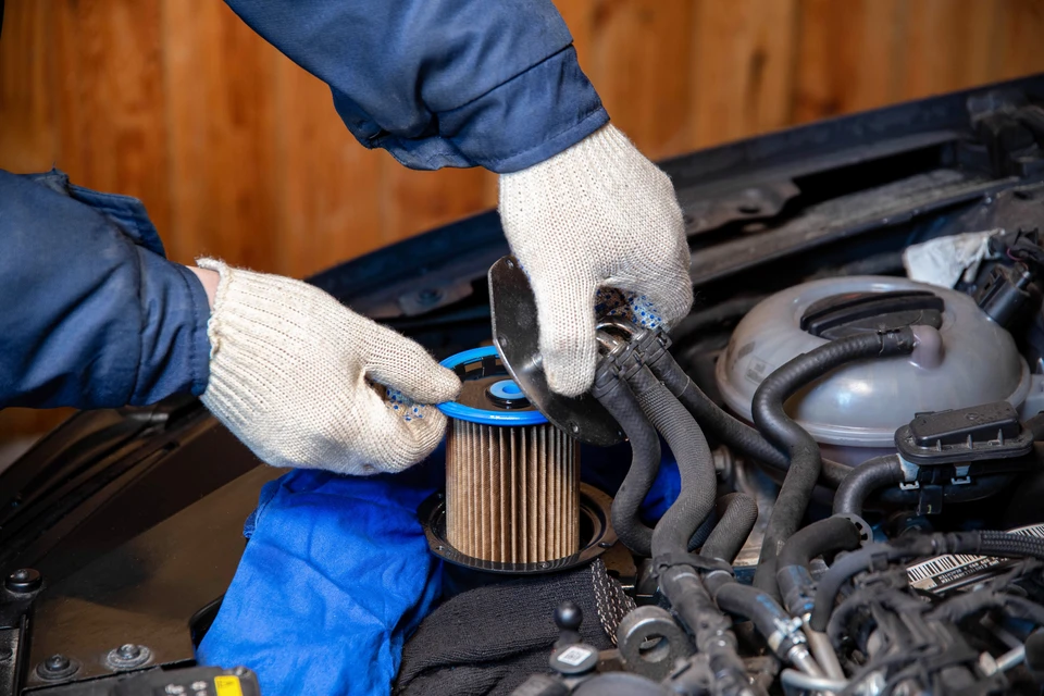 Mécanicien automobile en combinaison bleue et gants blancs remplace un filtre à huile cylindrique dans un moteur de véhicule